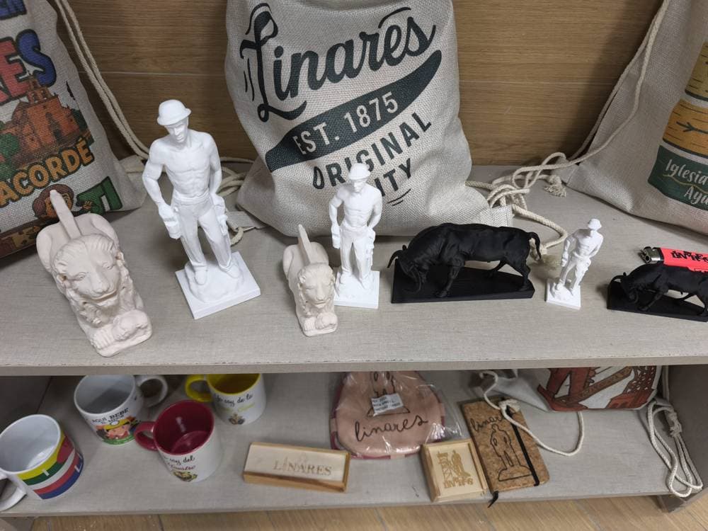 Figuras del Minero, León de Cástulo y toro junto a recuerdos de Linares en una estantería